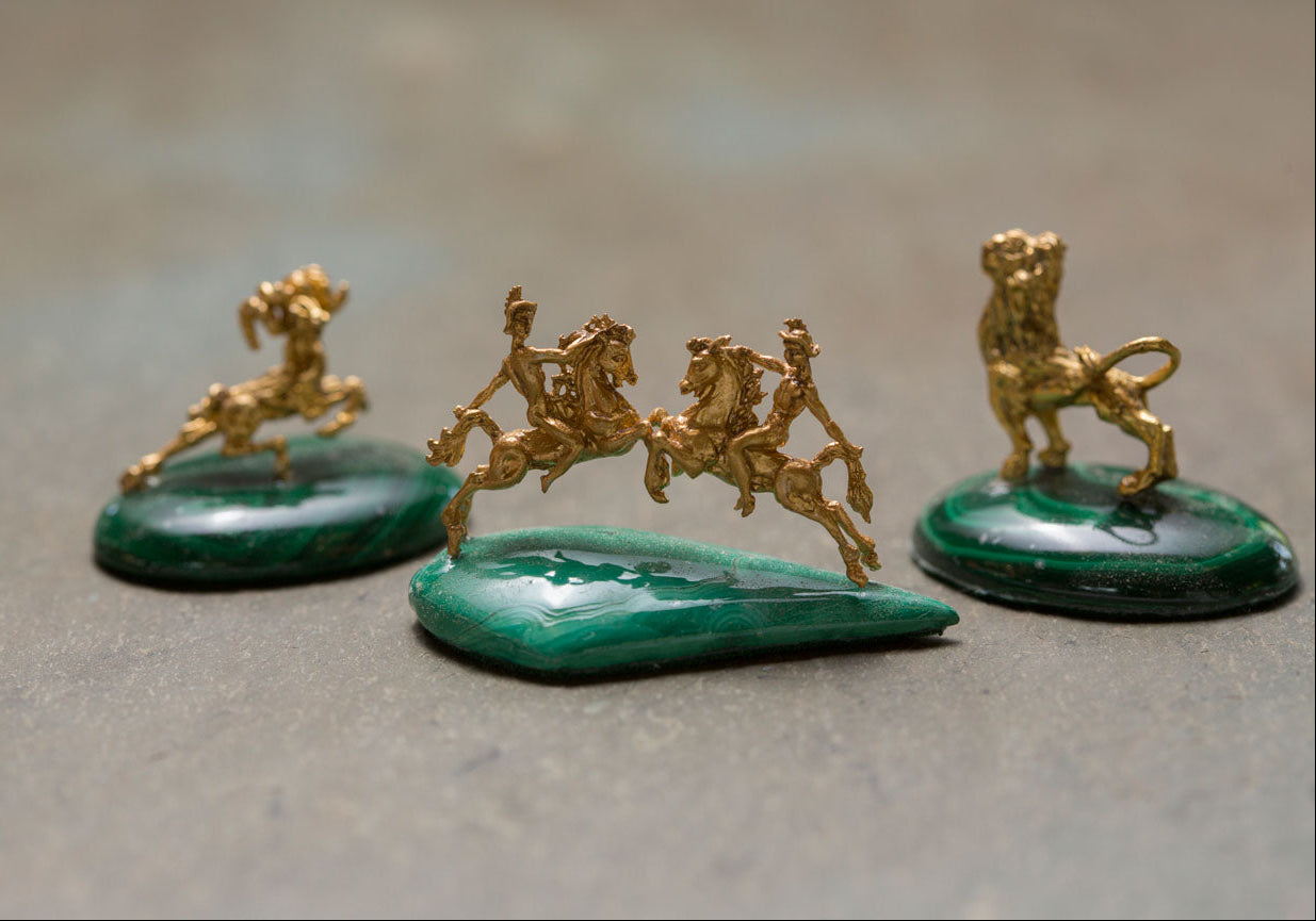 Three gold figurines on green stone bases on a gray surface